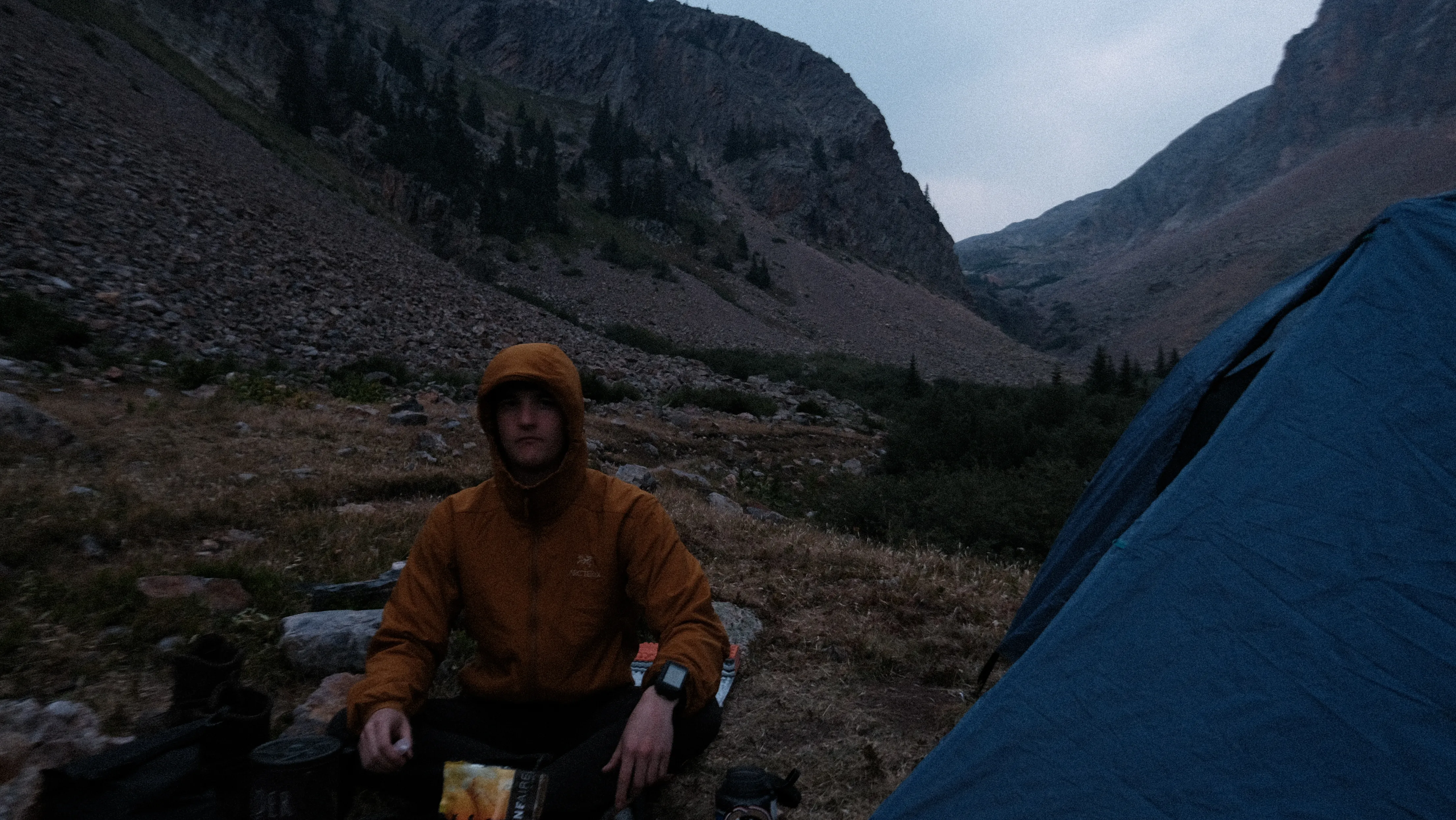At camp beside a blue tent in a rocky Colorado mountain valley